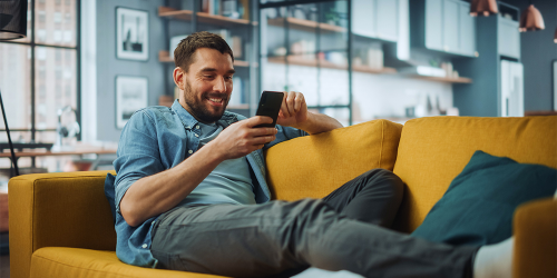 Ein Mann sitzt auf einem Sofa und schaut auf sein Handy.