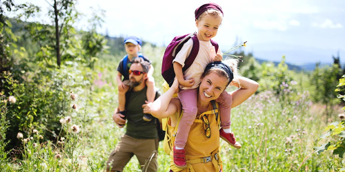 Junge Familie, die ihren Urlaub über Landsichten.de gebucht hat, wandert ausgelassen durch die ländliche Umgebung ihres Ferienhofs