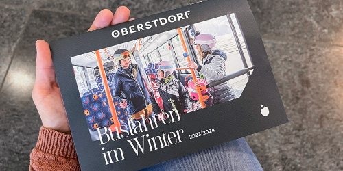 Eine Person hält die Busbroschüre von Oberstdorf in der Hand