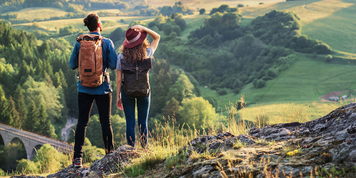 Zwei Wanderer mit Rucksäcken genießen die Aussicht auf ein weites Tal von einem Hügel in Baden-Württemberg aus.